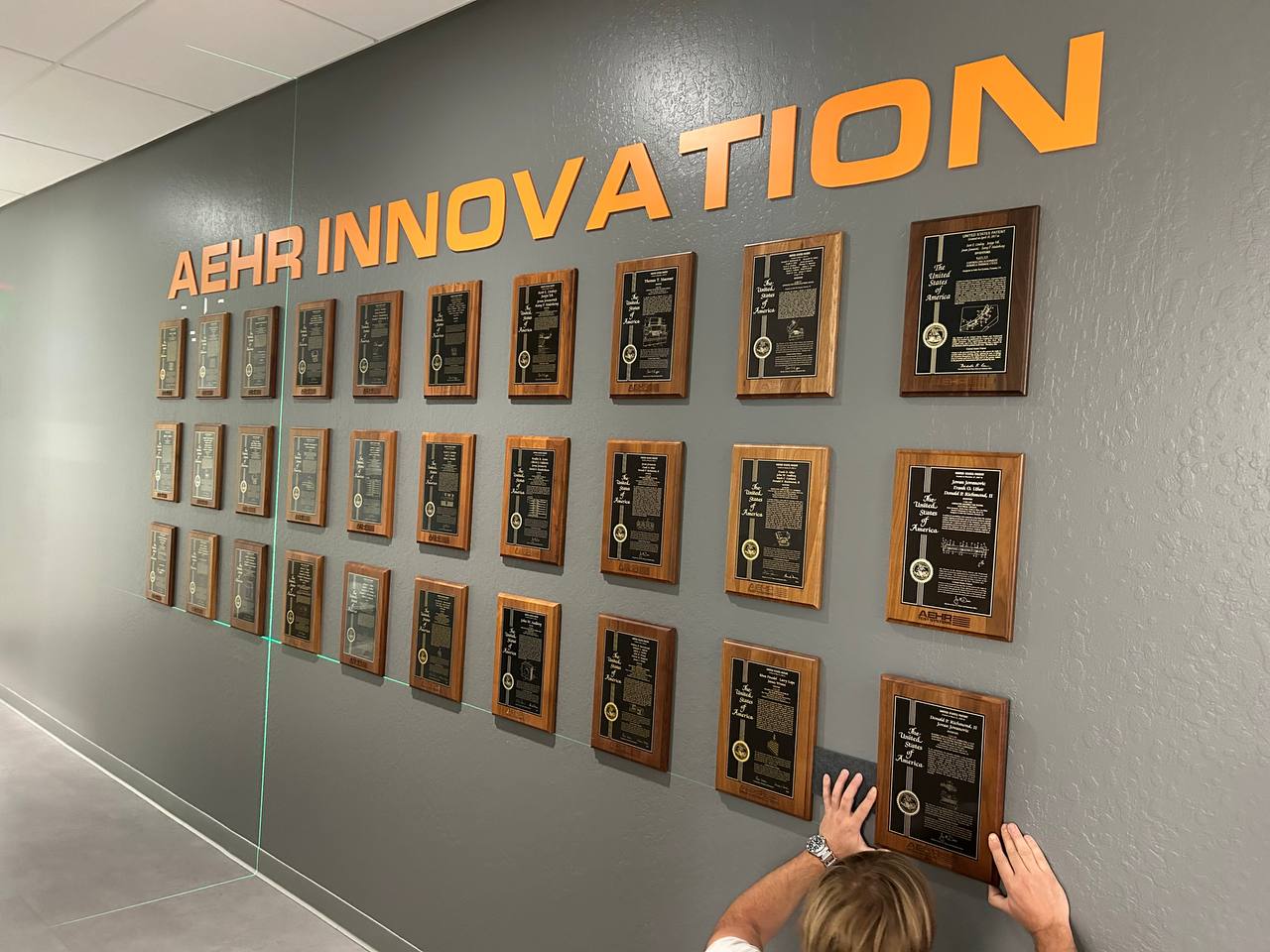 Installer mounting a framed patent plaque on an office feature wall