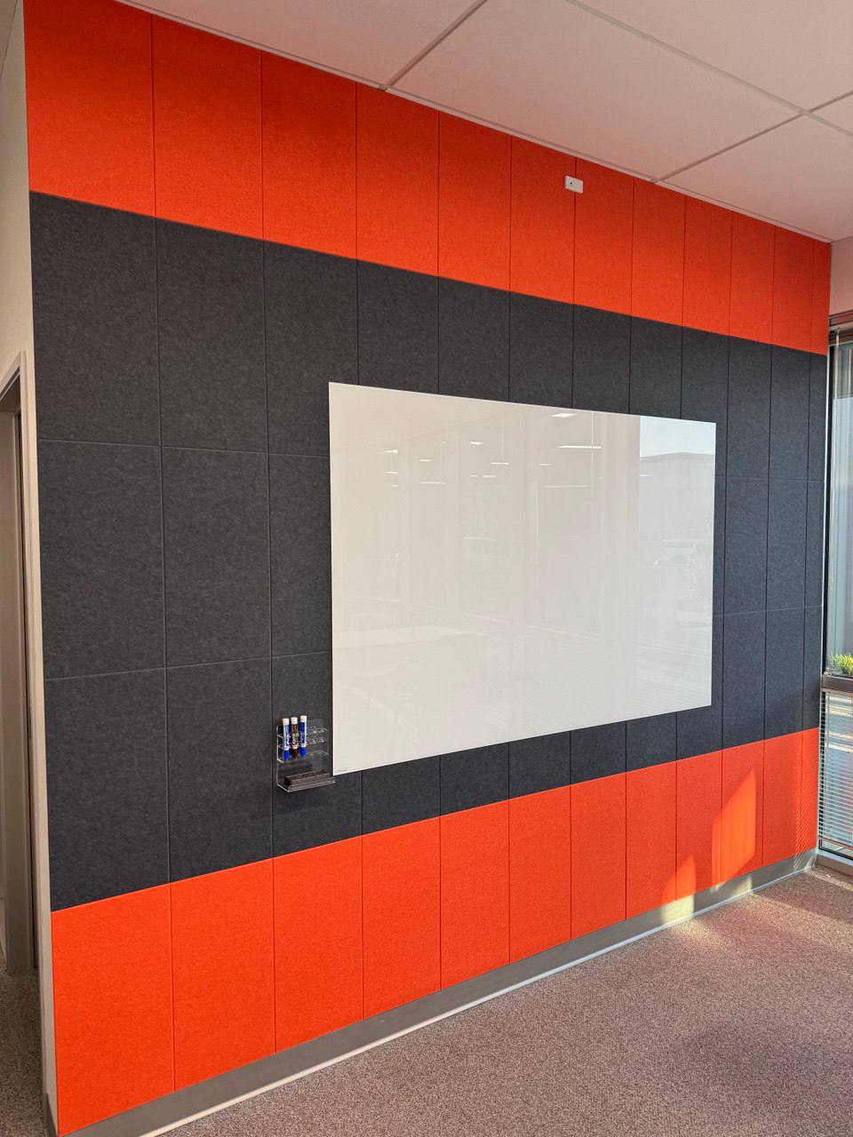 Orange and charcoal acoustic wall panels with a mounted whiteboard