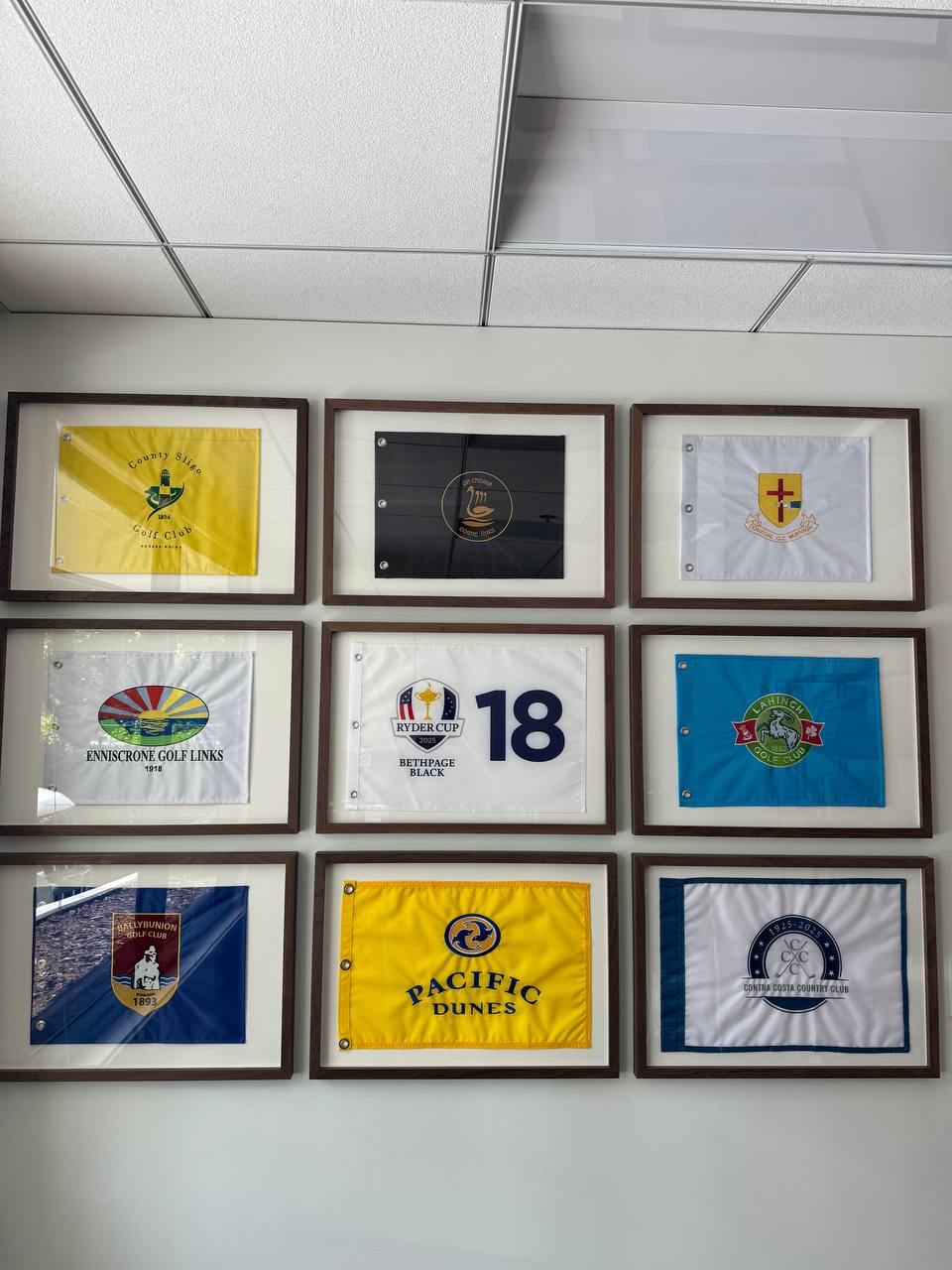 Nine framed golf flags arranged in a grid on an office wall
