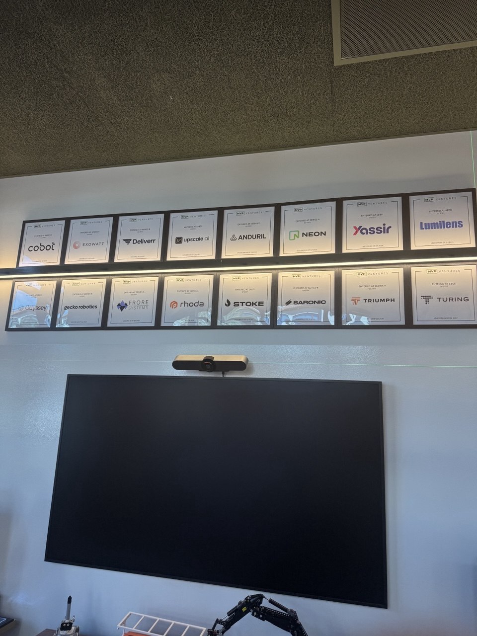 Two rows of framed company plaques mounted above a large wall display