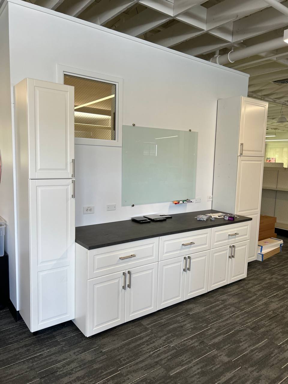 White storage cabinets and a mounted glass whiteboard in an open office