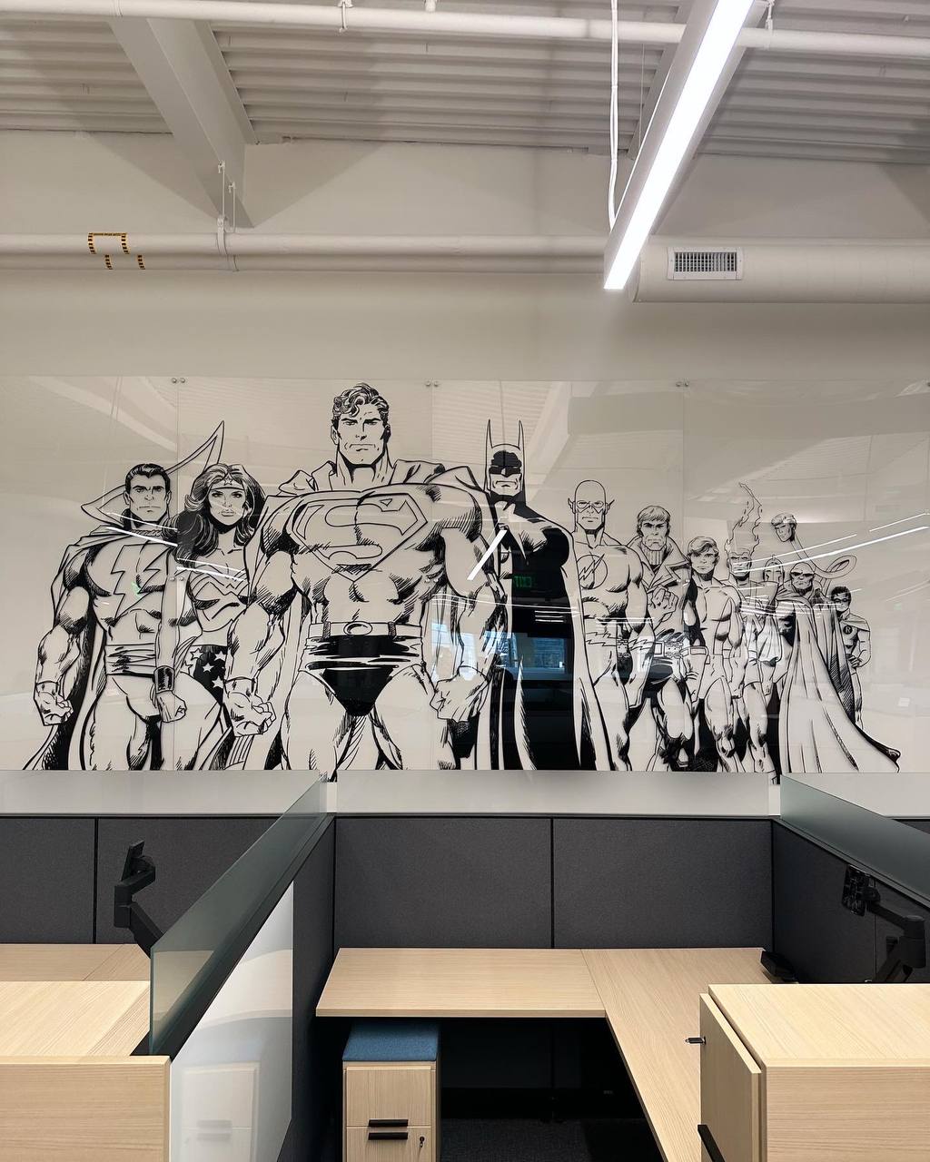 Glass partition panels with black-and-white superhero artwork above office workstations