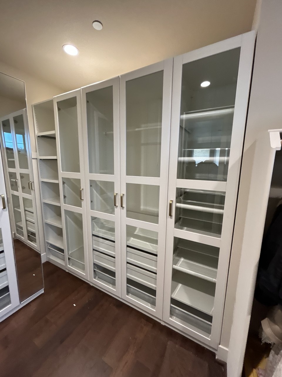 White glass-door wardrobes lining a walk-in closet